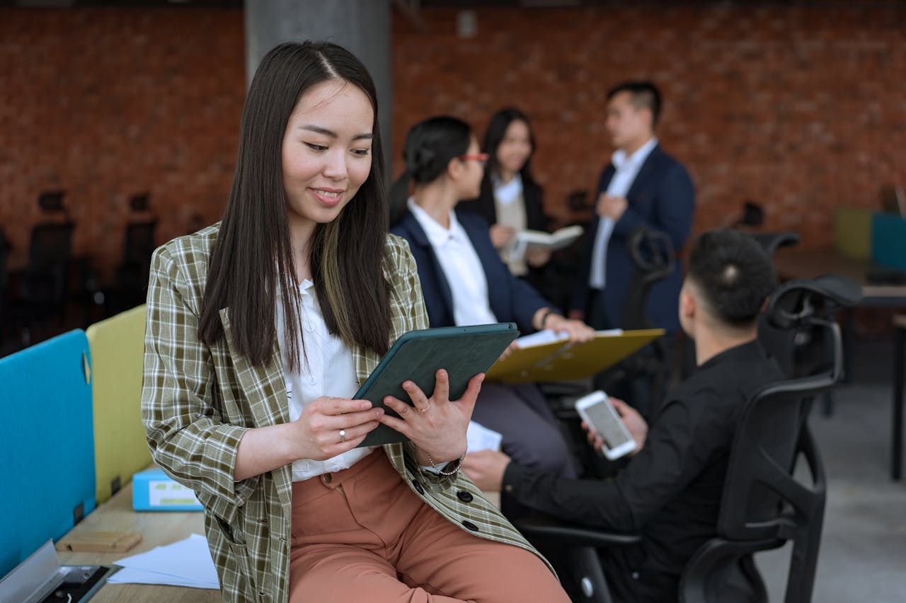Asian businesswoman using a tablet in a modern office setting with colleagues.